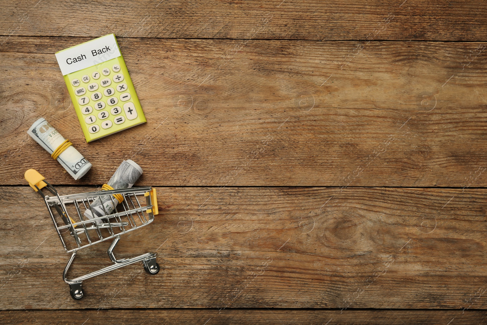 Photo of Calculator, rolled dollar banknotes and shopping cart on wooden background, flat lay with space for text. Cashback concept