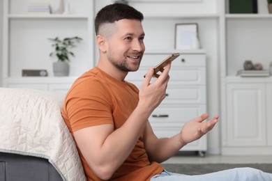 Photo of Handsome man recording voice message via smartphone at home