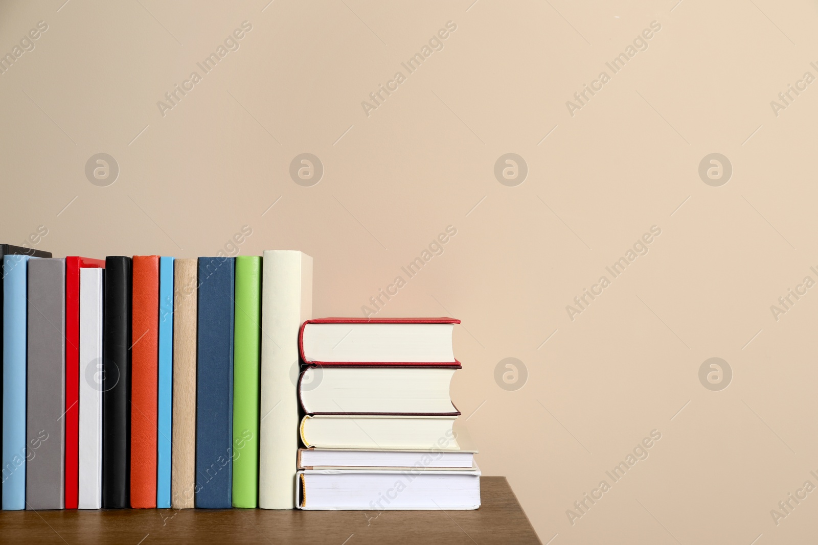 Photo of Many different hardcover books on wooden table near beige wall. Space for text