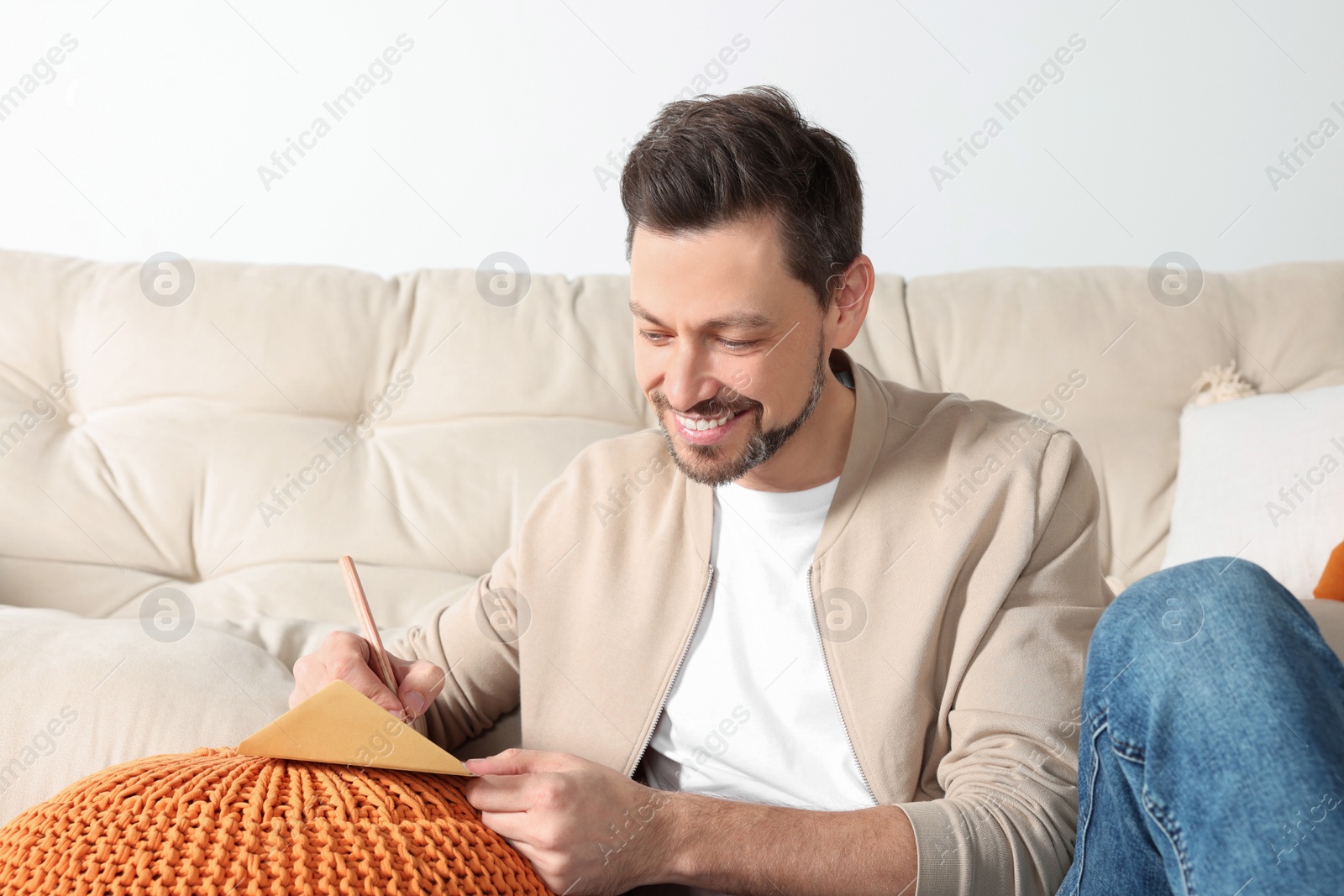 Photo of Happy man writing message in greeting card in living room