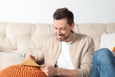 Happy man writing message in greeting card in living room