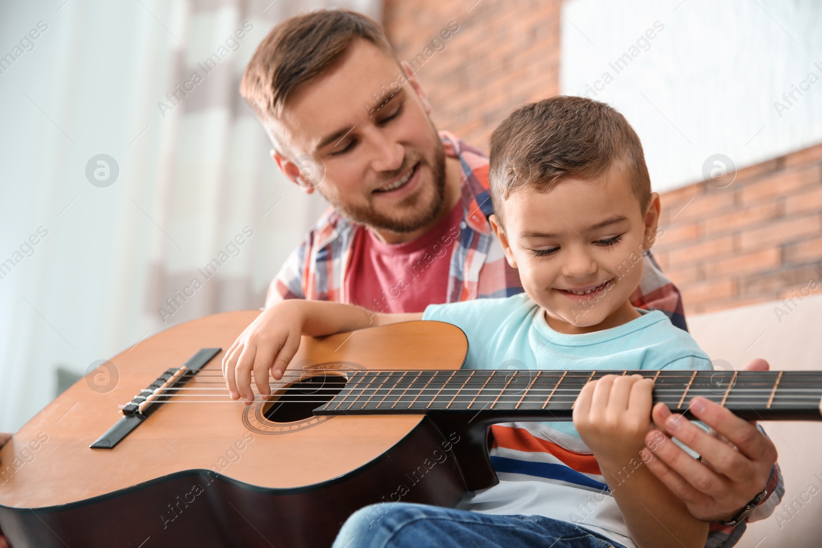 Photo of Father teaching his little son to play guitar at home