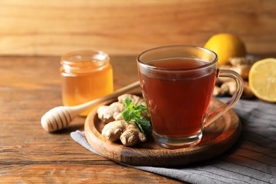 Cup of delicious ginger tea and ingredients on wooden table, space for text