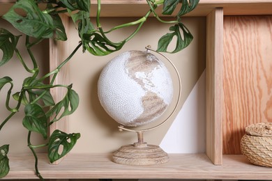 Photo of Wooden shelving unit with stylish globe and houseplant on color wall. Interior accessories