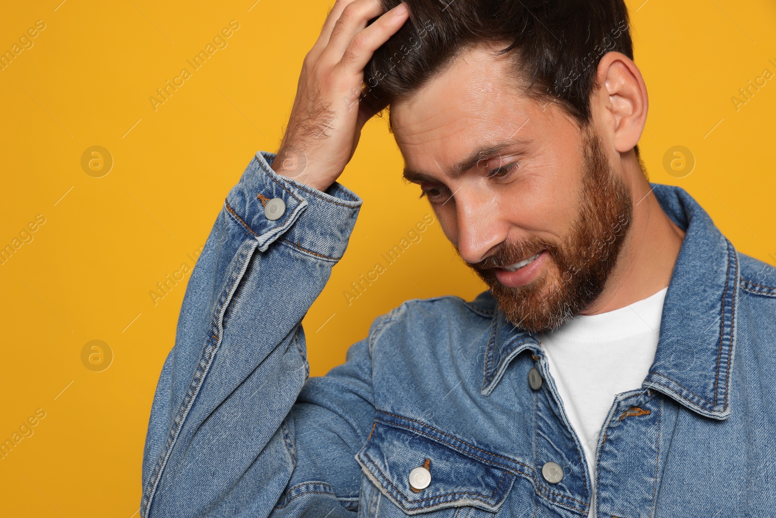 Photo of Bearded man fixing hair on orange background