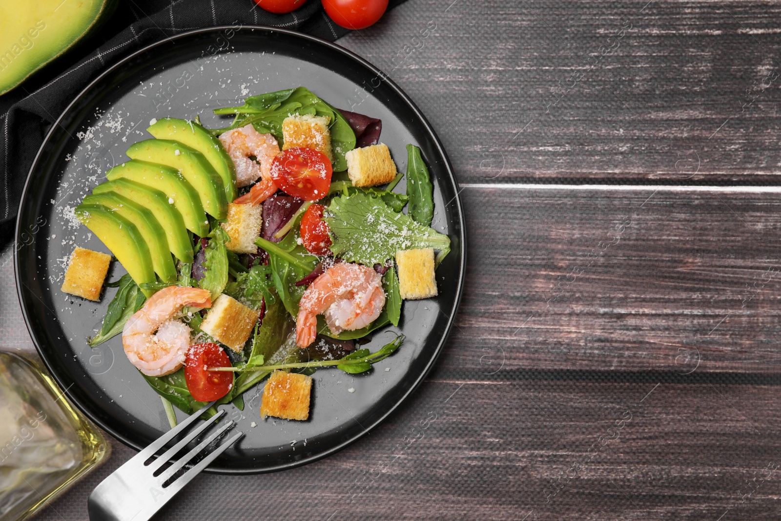 Photo of Delicious salad with croutons, avocado and shrimp served on wooden table, flat lay. Space for text