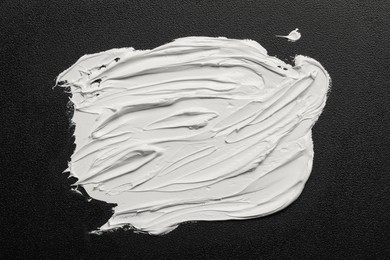 Strokes of white oil paint on black canvas, top view