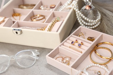 Photo of Jewelry boxes with many different accessories, glasses and perfume on light grey table, closeup