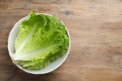 Photo of Bowl with fresh leaves of green romaine lettuce on wooden table, top view. Space for text