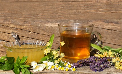 Cup of hot aromatic tea, honey and different fresh herbs on wooden table