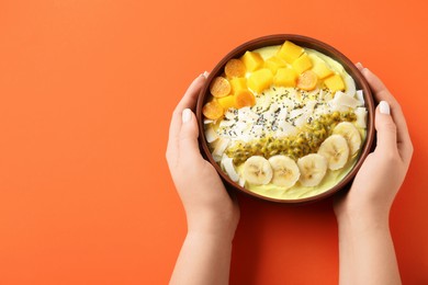 Woman holding tasty smoothie bowl with fresh fruits at orange table, top view. Space for text