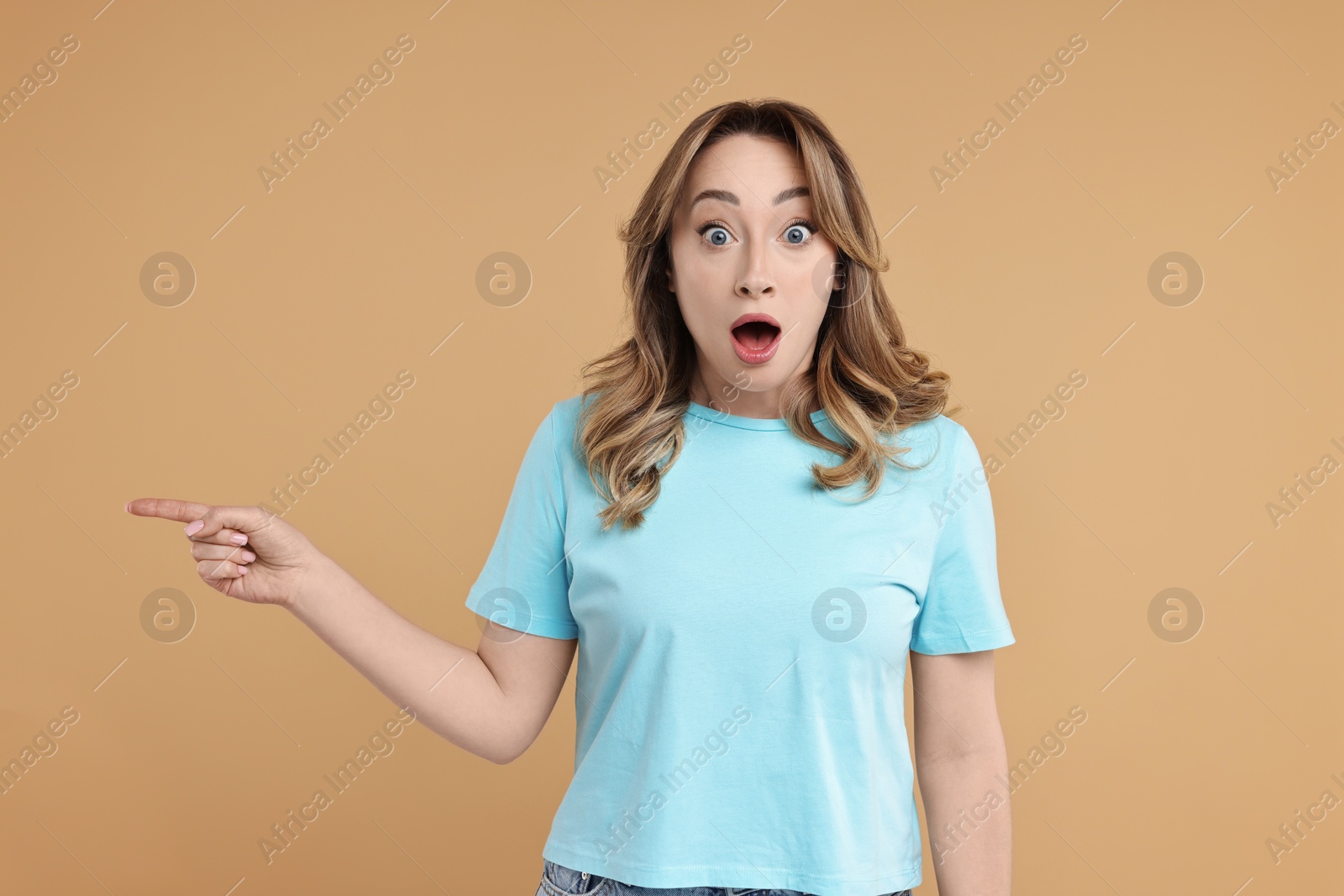 Photo of Portrait of surprised woman pointing at something on beige background