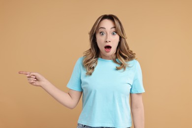 Portrait of surprised woman pointing at something on beige background