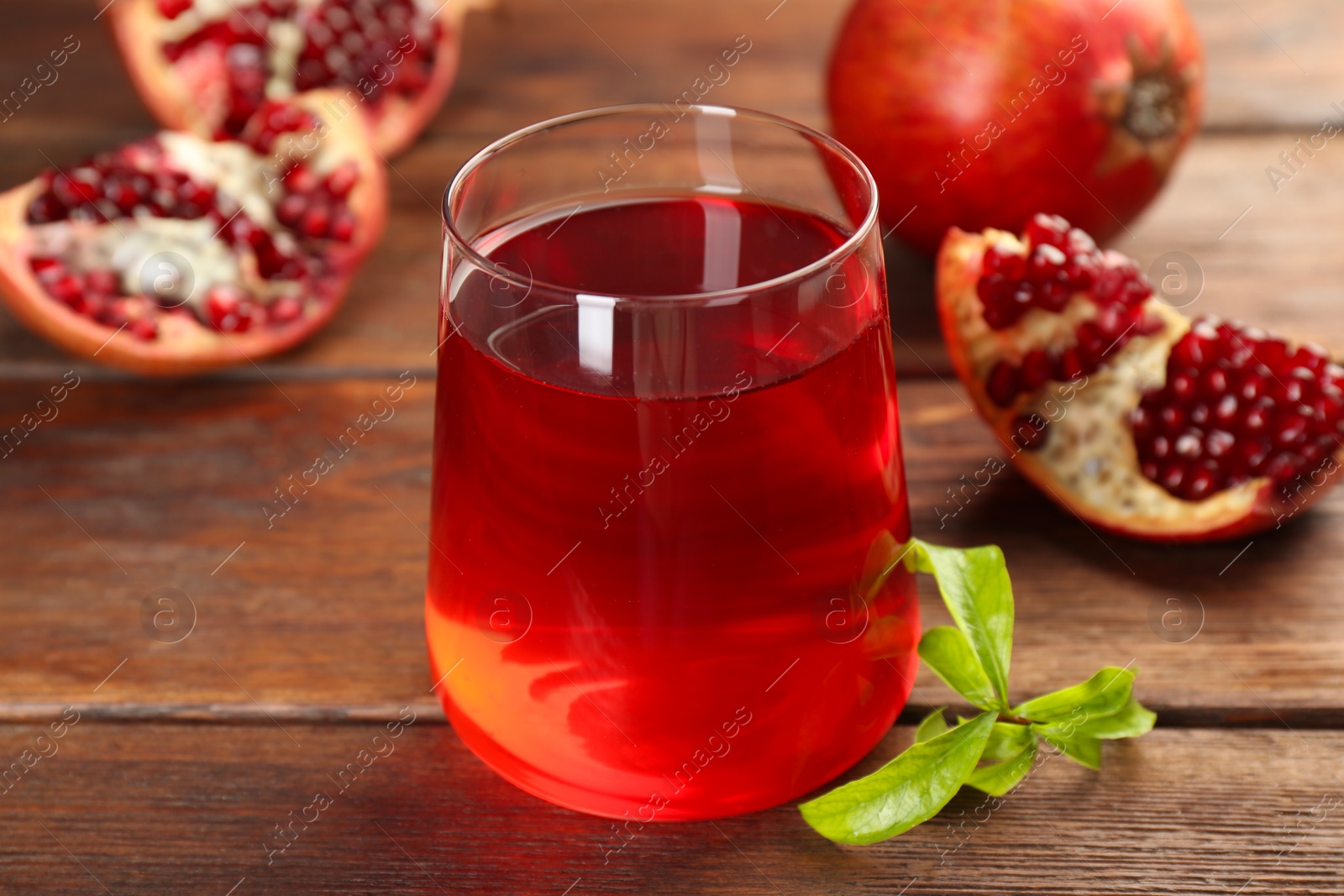 Photo of Tasty pomegranate juice in glass and fresh fruits on wooden table, closeup