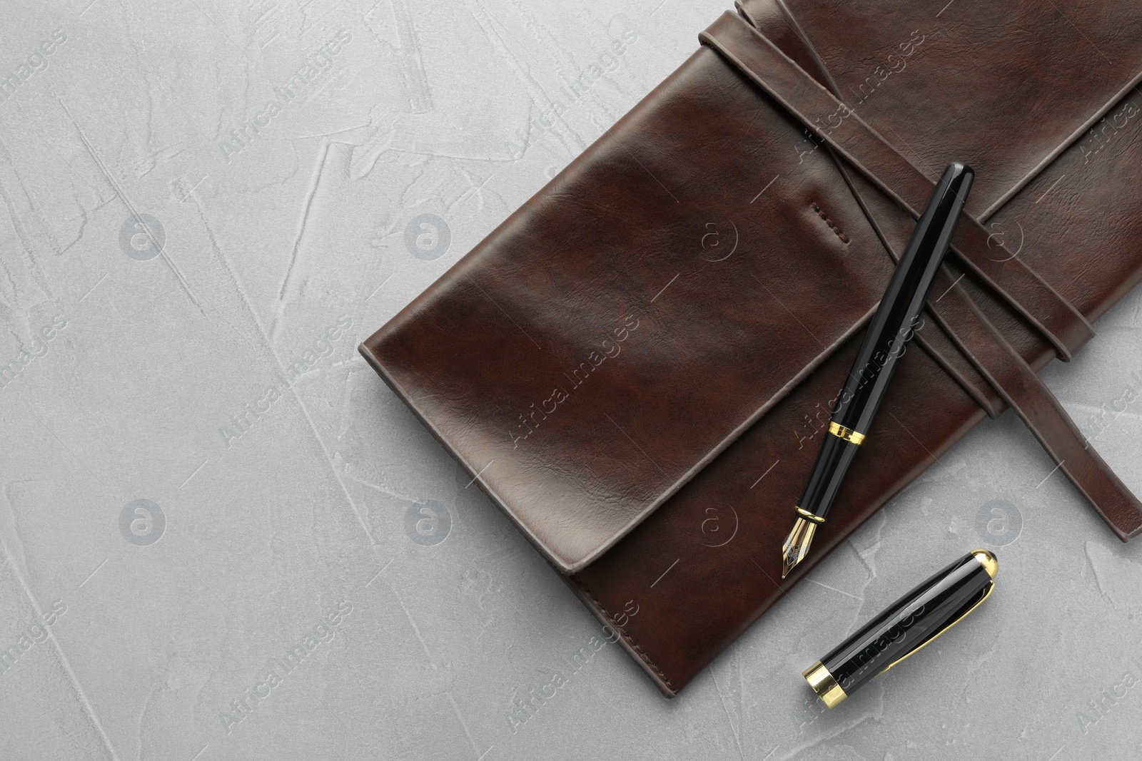 Photo of Stylish fountain pen, cap and leather notebook on light grey textured table, flat lay. Space for text