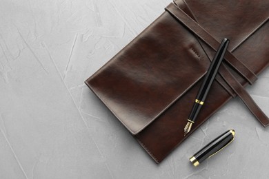 Photo of Stylish fountain pen, cap and leather notebook on light grey textured table, flat lay. Space for text