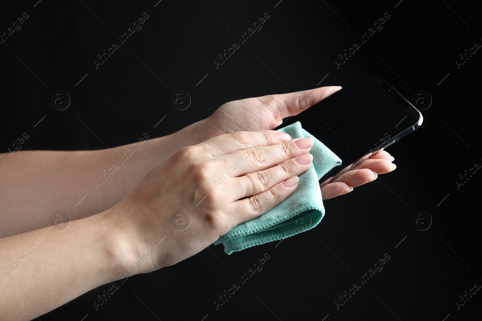 Photo of Woman cleaning smartphone with microfiber cloth against black background, closeup