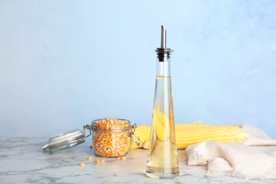 Photo of Bottle of corn oil and fresh cobs on table against color wall