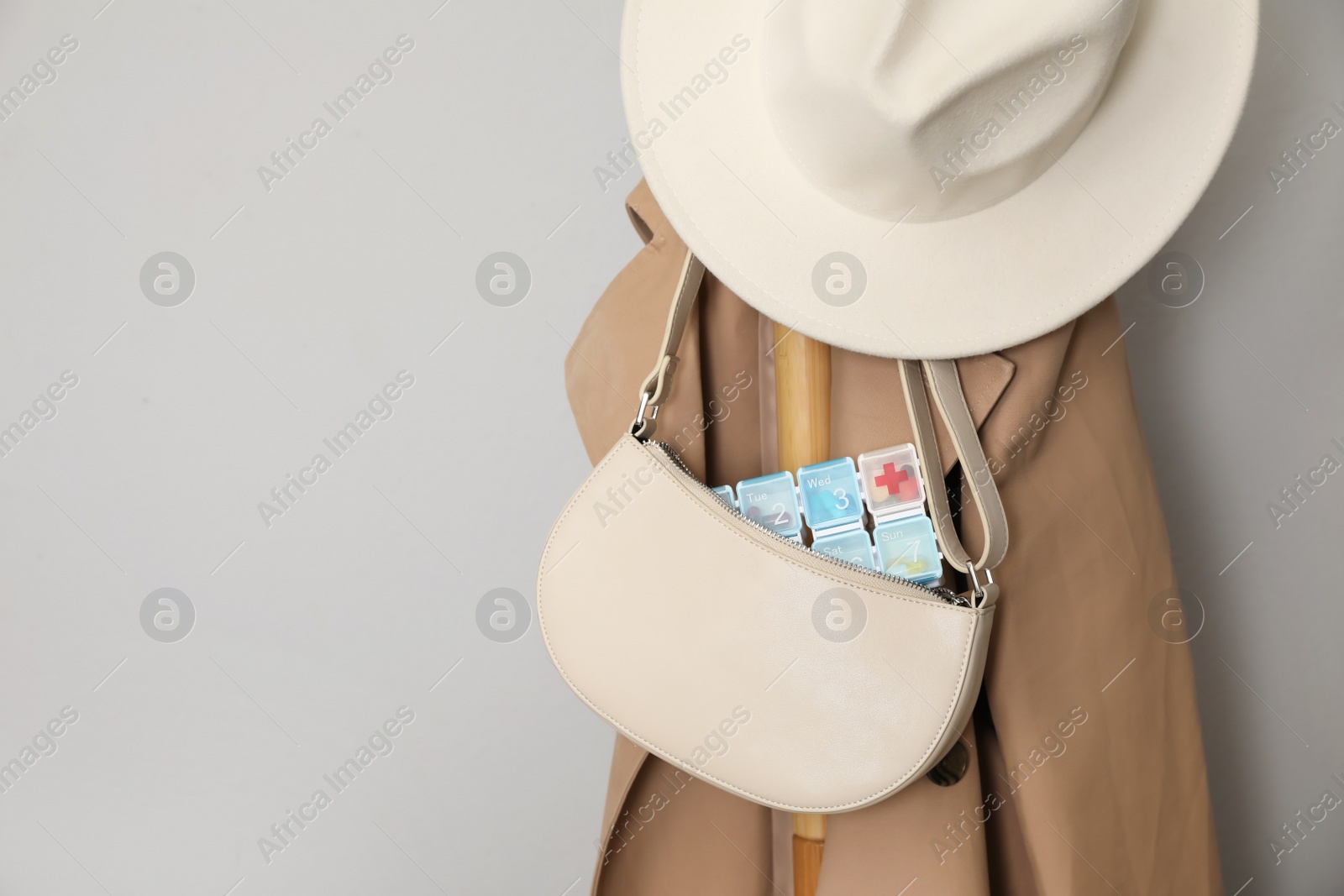 Photo of Stylish women's bag with plastic pill box hanging on stand near light grey wall. Space for text