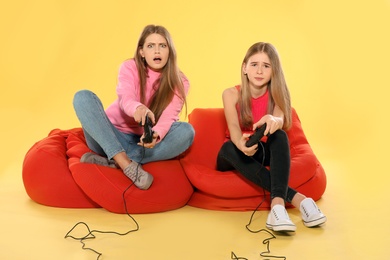 Young woman and teenage girl playing video games with controllers on color background