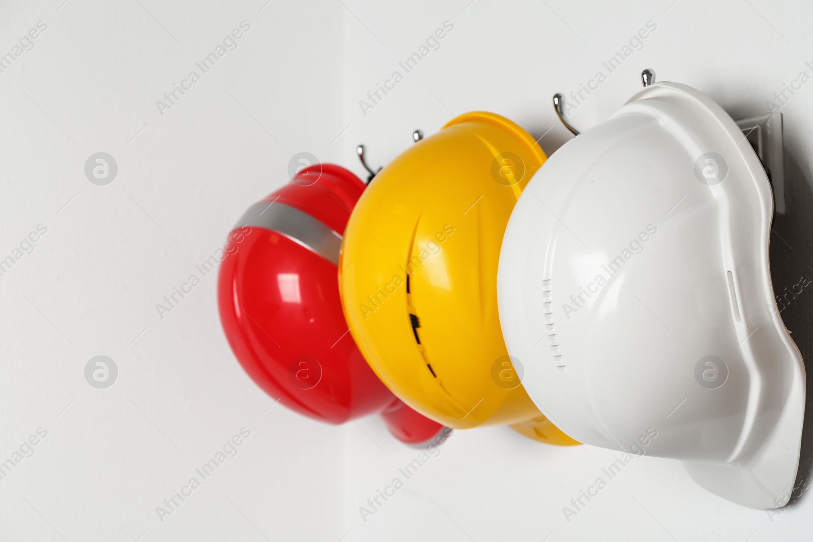 Photo of Hard hats hanging on white wall. Safety equipment