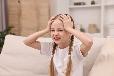 Photo of Little girl suffering from headache on sofa indoors