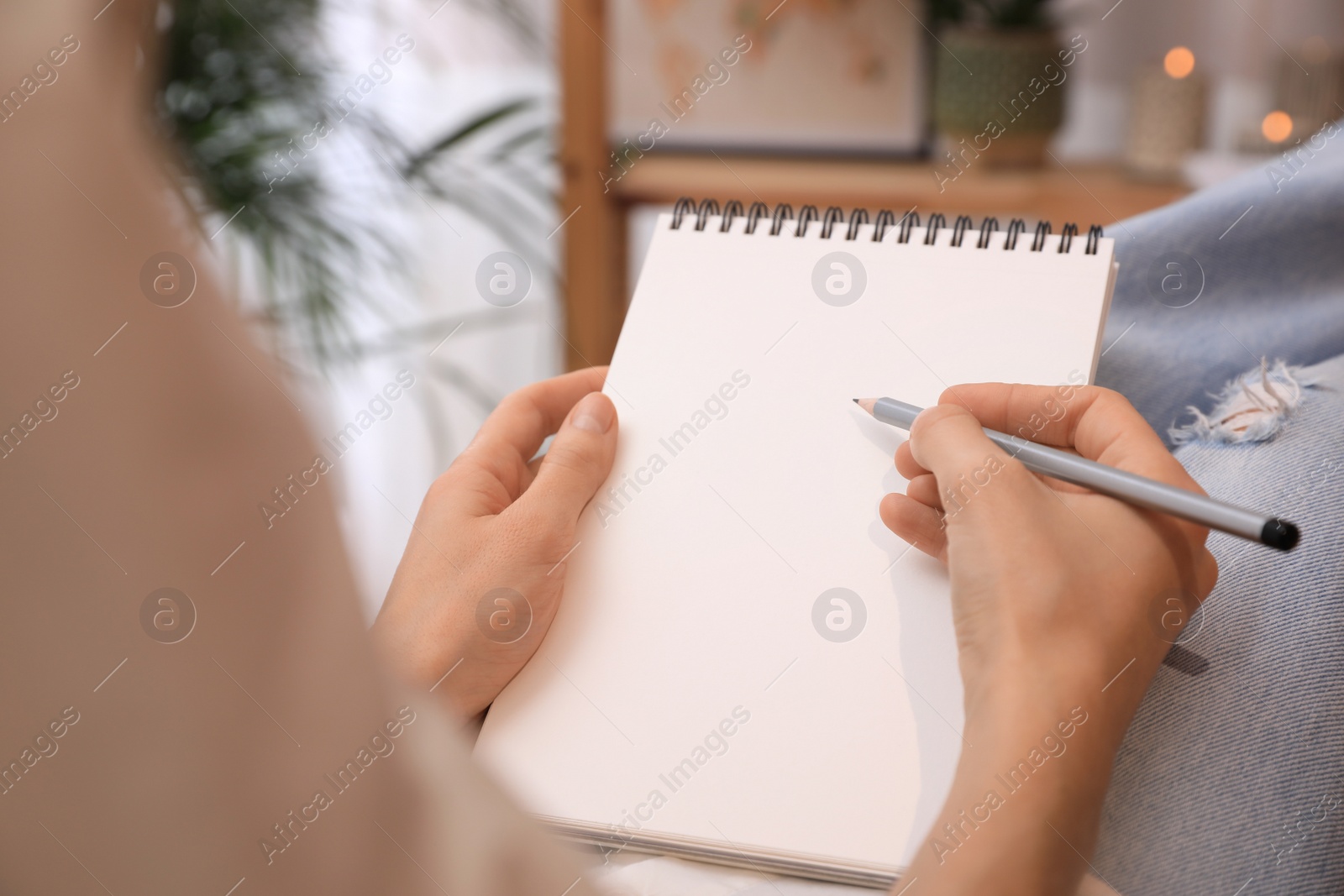 Photo of Woman drawing in sketchbook with pencil at home, closeup