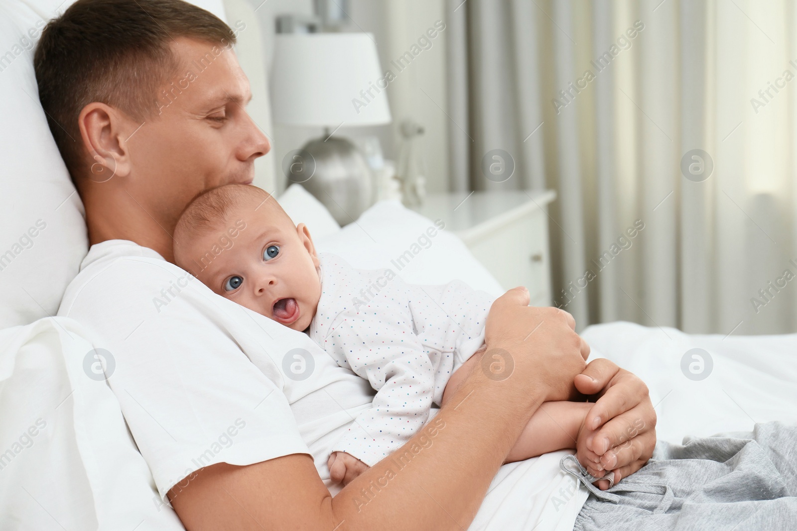 Photo of Father holding his cute baby on bed at home, space for text