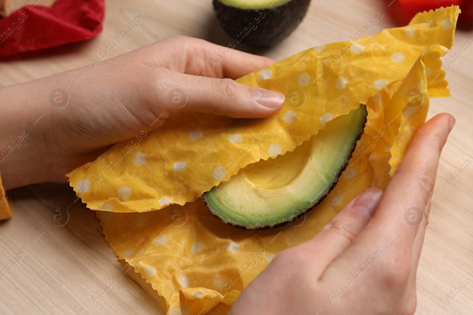 Photo of Woman packing half of fresh avocado into beeswax food wrap at wooden table, closeup