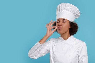 Photo of Happy female chef in uniform showing perfect sign on light blue background. Space for text