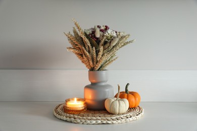 Photo of Beautiful bouquet of dry flowers, small pumpkins and candle on white table near light wall