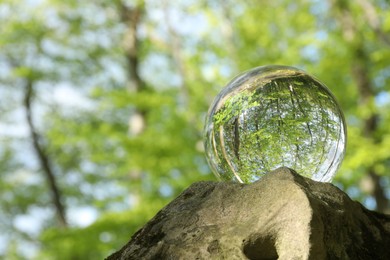 Beautiful green trees outdoors, overturned reflection. Crystal ball on stone in forest. Space for text