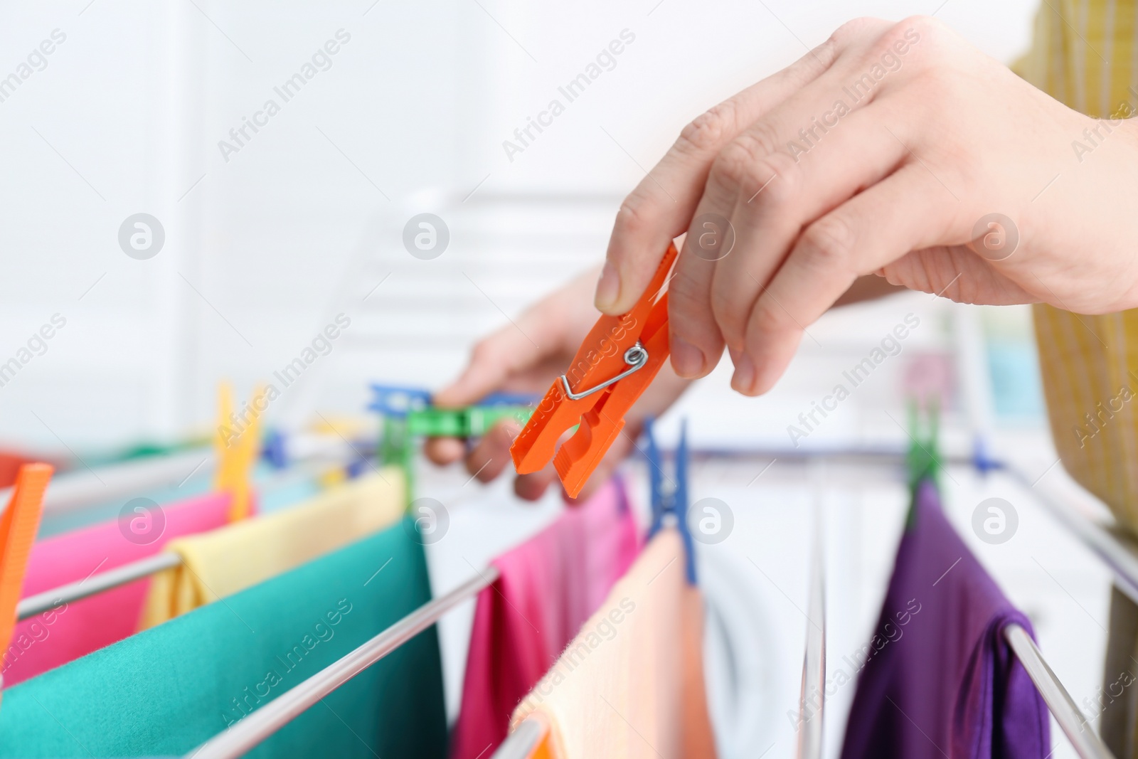 Photo of Woman hanging clean laundry on drying rack indoors, closeup