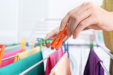 Photo of Woman hanging clean laundry on drying rack indoors, closeup