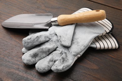 Pair of color gardening gloves and trowel on wooden table, closeup