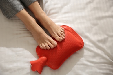 Woman warming feet with hot water bottle on bed, closeup