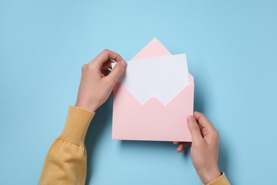 Photo of Woman taking card out of letter envelope at light blue table, top view