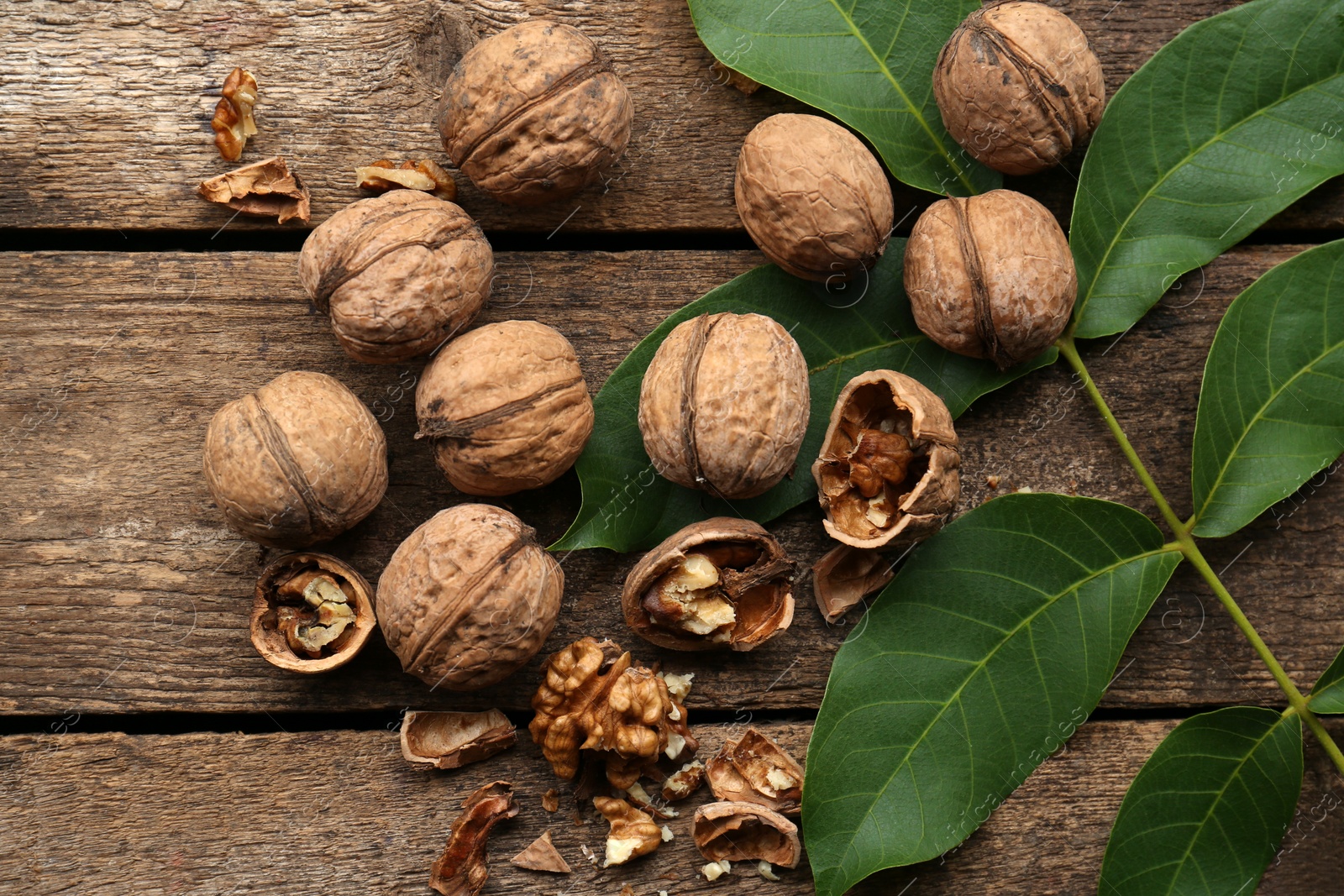 Photo of Whole and cracked walnuts with green leaves on wooden table, flat lay