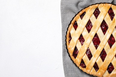 Delicious fresh cherry pie and grey towel on white table, top view. Space for text