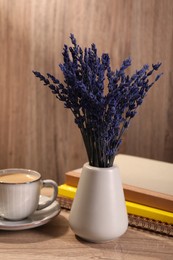 Photo of Bouquet of beautiful preserved lavender flowers, notebooks and cup of coffee on wooden table indoors