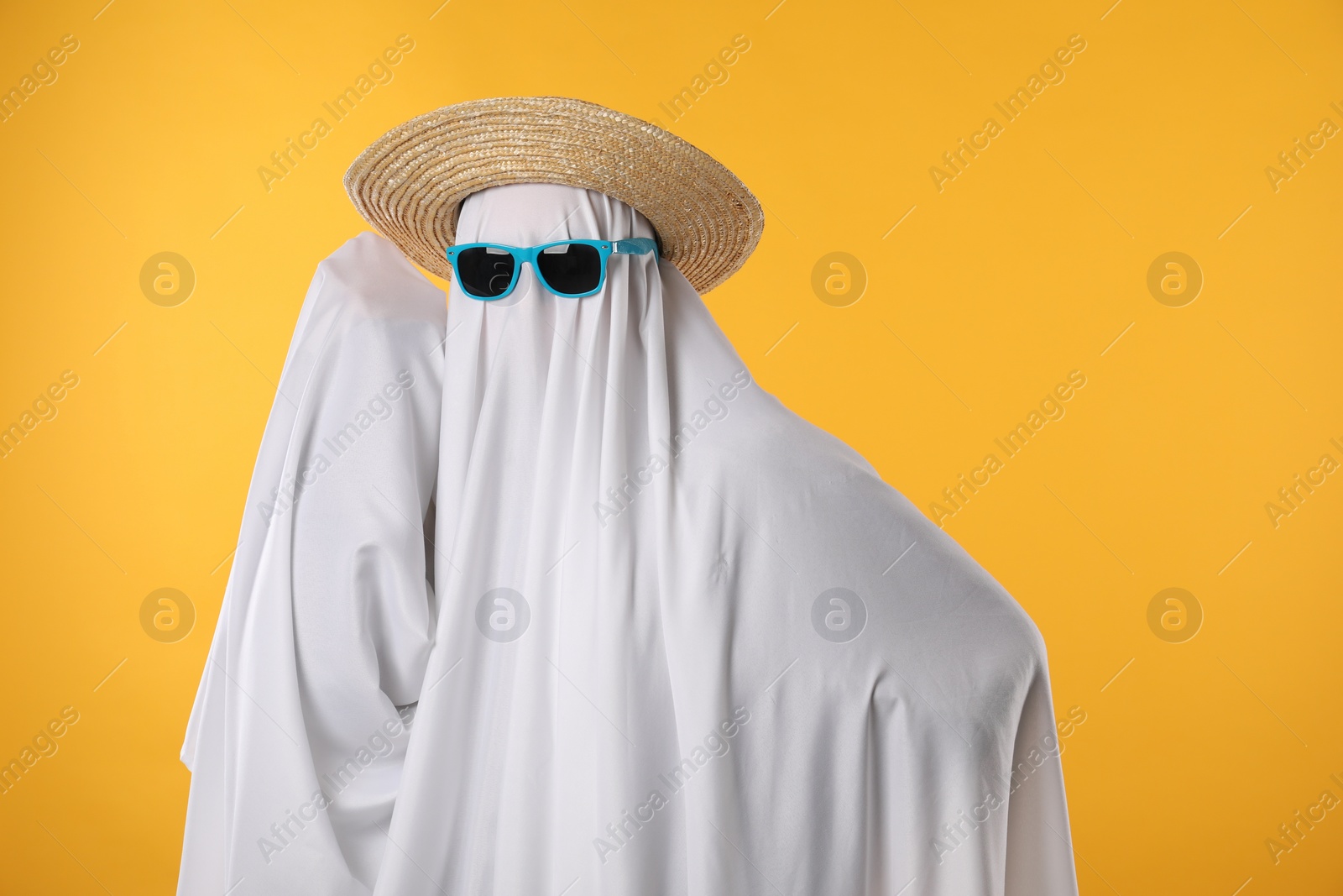 Photo of Person in ghost costume, sunglasses and straw hat on yellow background, space for text