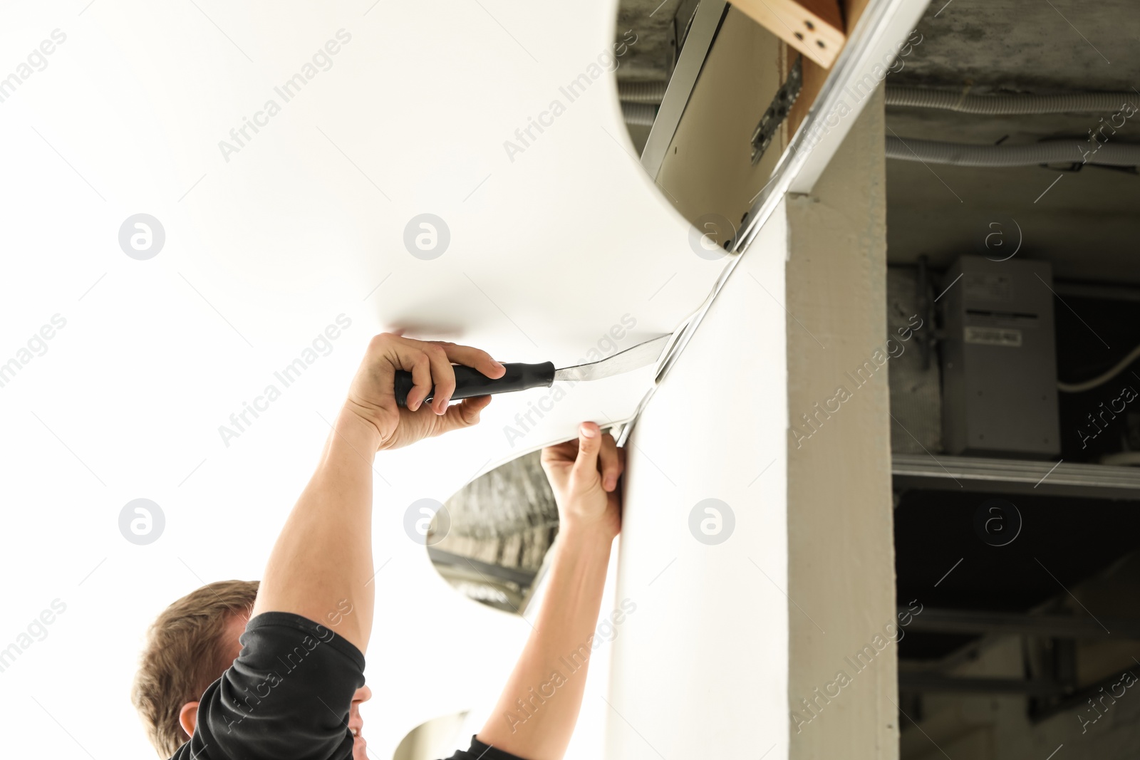 Photo of Repairman installing white stretch ceiling in room, closeup