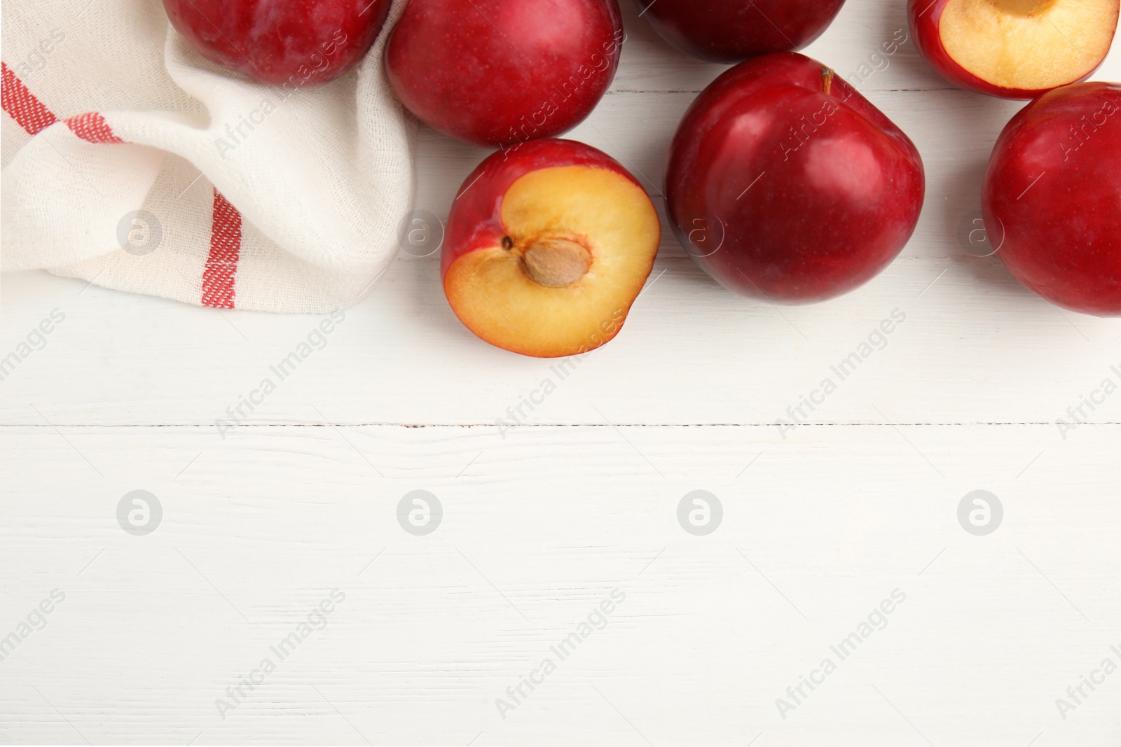 Photo of Delicious ripe plums on white wooden table, flat lay. Space for text