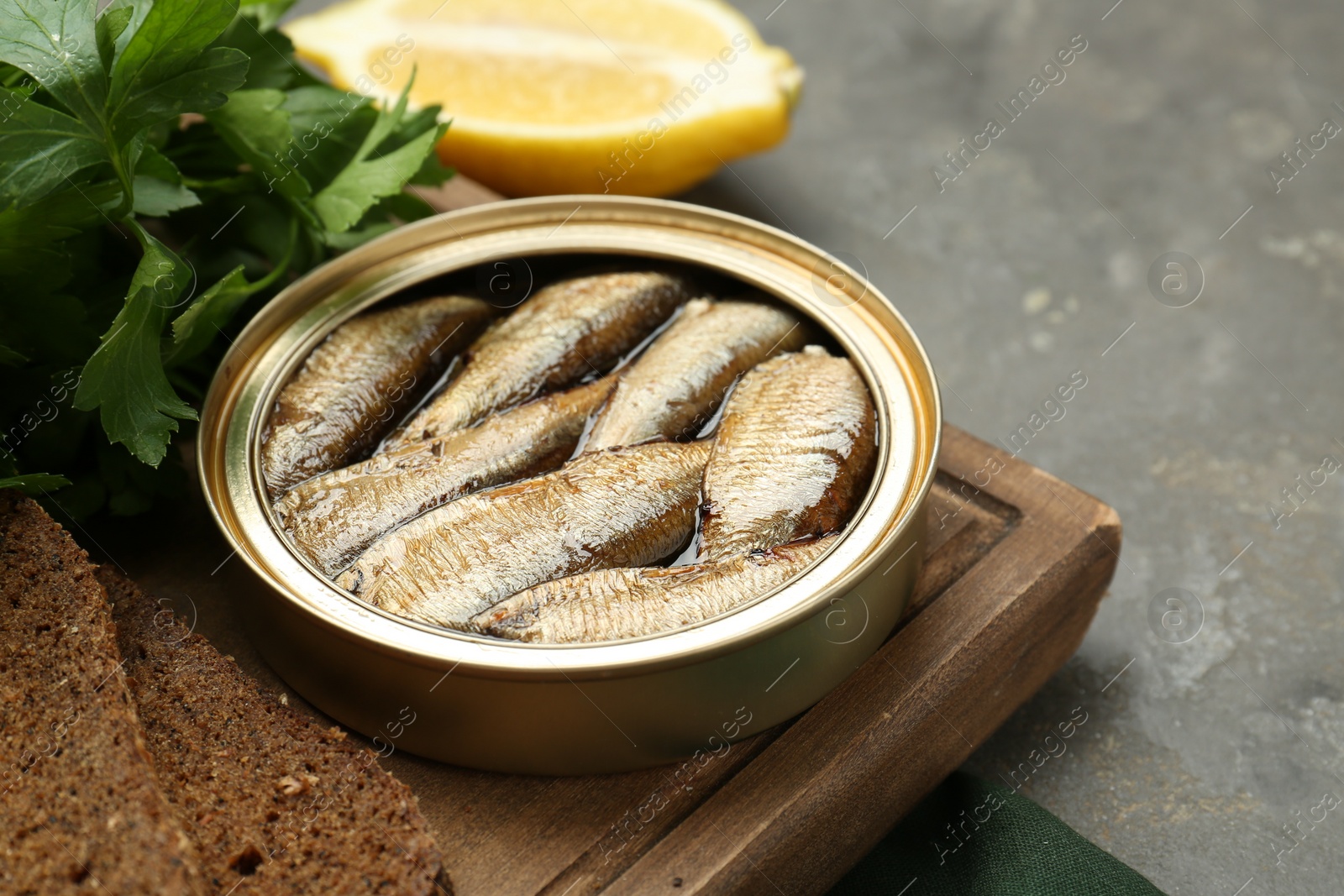 Photo of Tin can with tasty sprats served on grey textured table, closeup