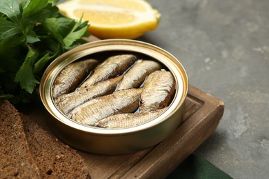 Photo of Tin can with tasty sprats served on grey textured table, closeup