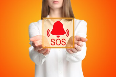 Young woman holding virtual icon SOS on orange background, closeup