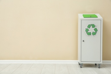 Photo of Trash bin with recycling symbol near color wall indoors. Space for text