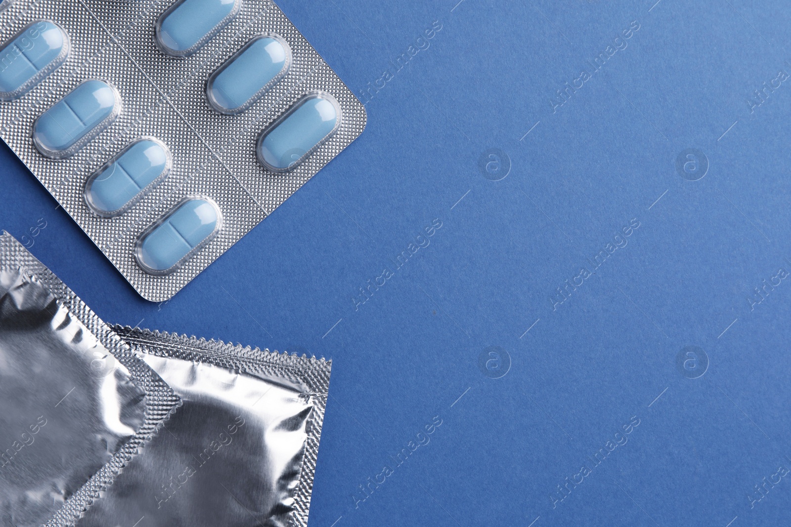 Photo of Pills and condoms on blue background, flat lay with space for text. Potency problem