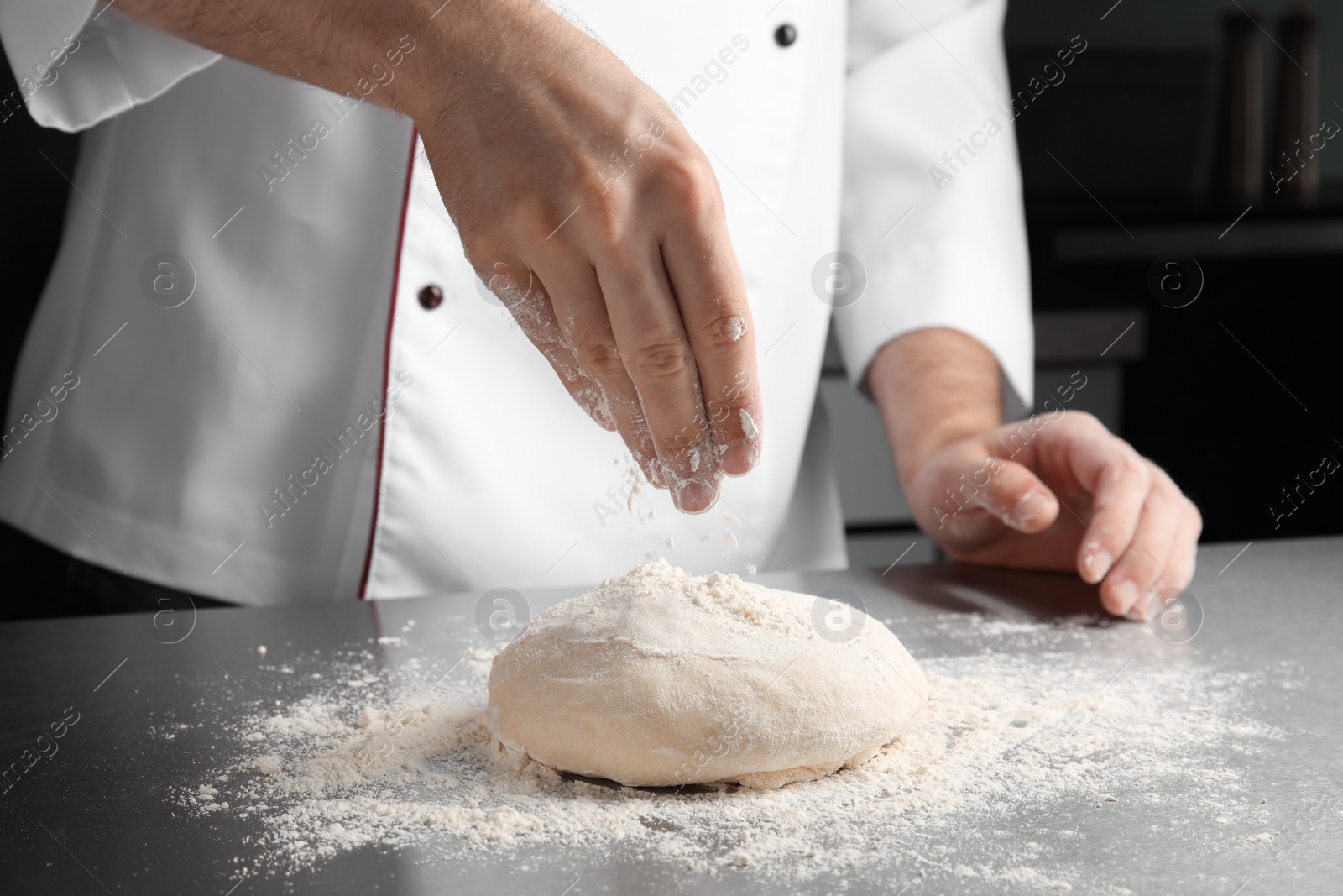 Photo of Man sprinkling dough for pastry with flour on table