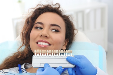 Dentist matching patient's teeth color with palette in office